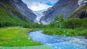 A river flowing between mountains, surrounded by green grass.